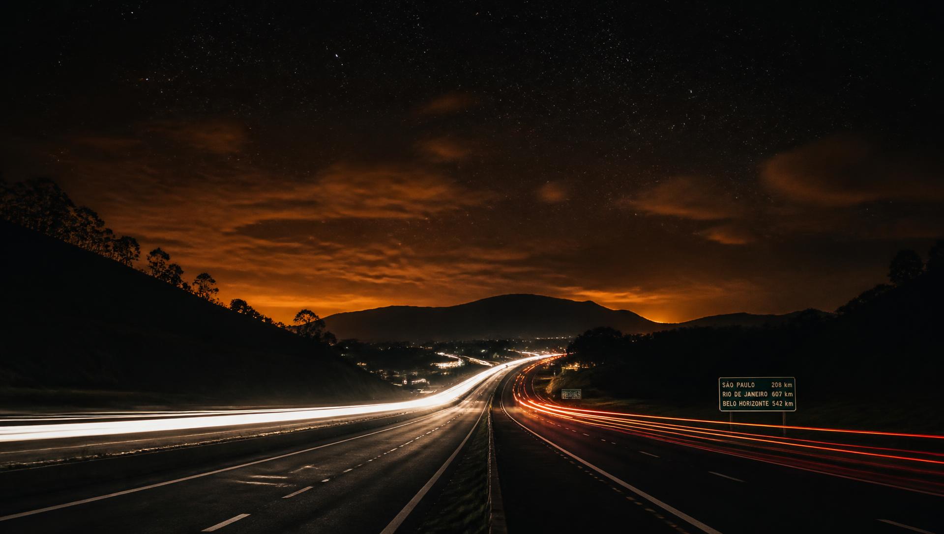 Estrada à noite com luzes de carro e céu estrelado